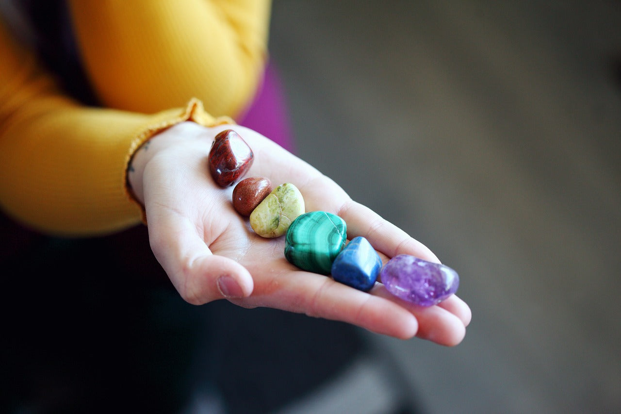 A hand holding seven different crystals, each one for a different chakra