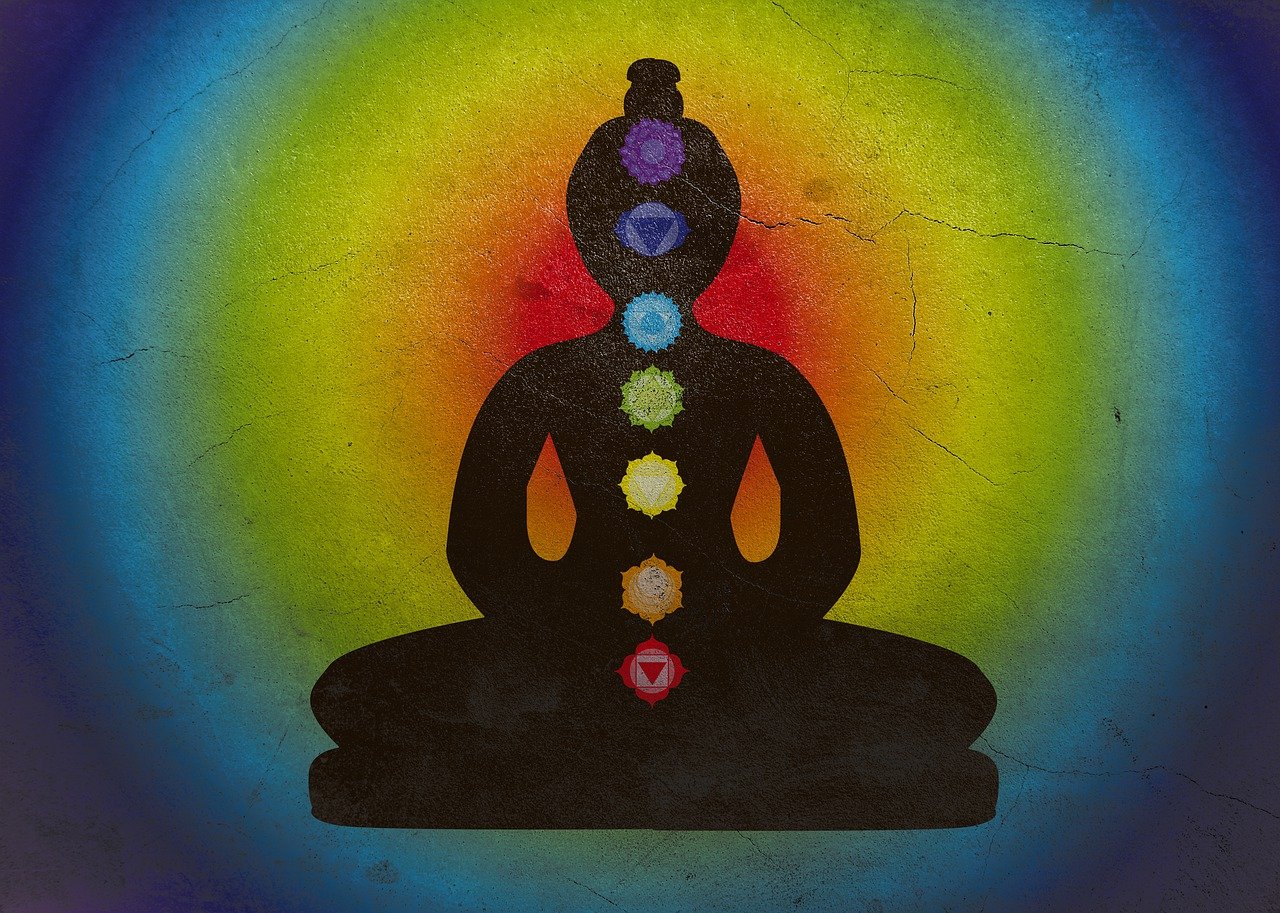 A black figured Buddha siting in a meditated stage with the seven chakras going up the middle of the figure. Around the figure is a glowing radiating colors of light