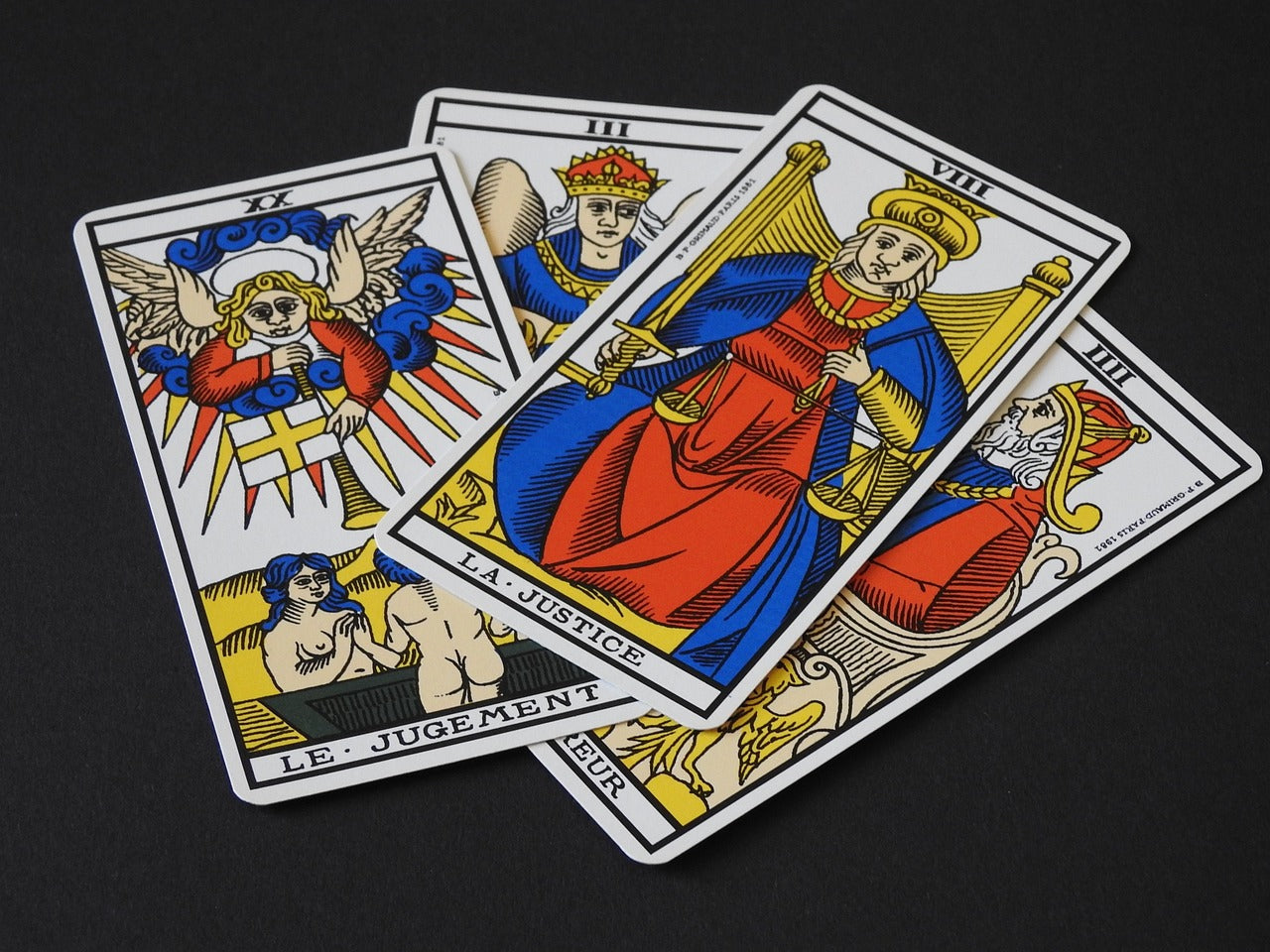 Four major arcana tarot cards face up on a black background. The cards are from an older style of tarot cards with Justice and Judgment being the two of the four cards you can see clearly in the image.