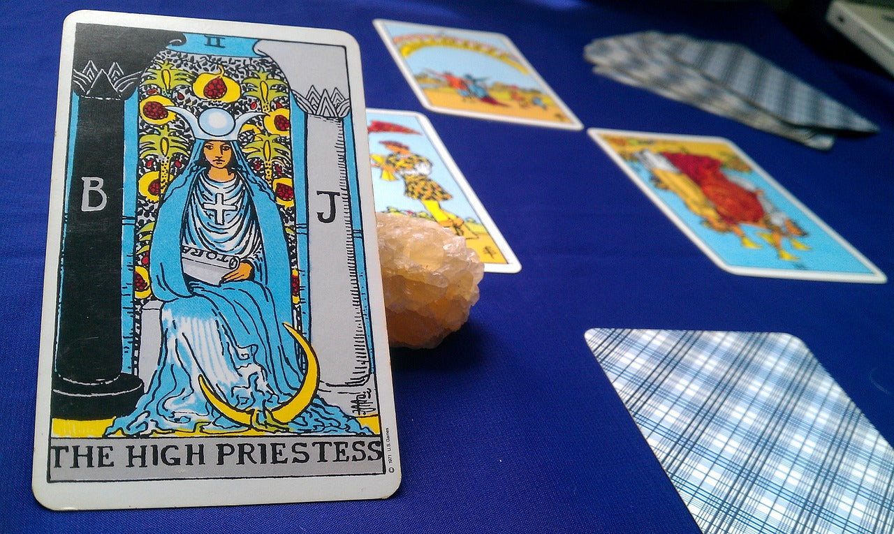 Tarot cards laid out in a spread with four cards turned over an one card not turned over. One card is reversed and the rest are facing forward. The closest card is the High Priestess