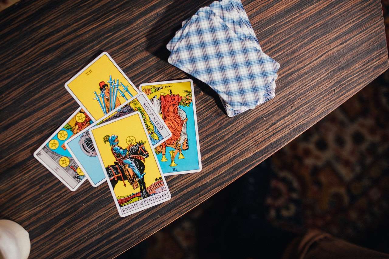 Five tarot cards in a pile to the left all upright and the rest of the deck face down to the right. They are on a dark brown table.