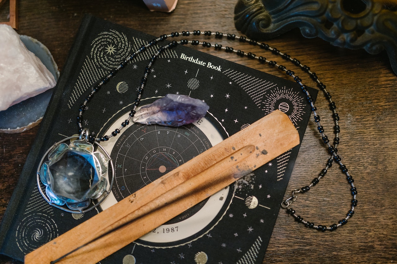 An incense burner, candle holder and a amethyst necklace on top of a birth cart book.