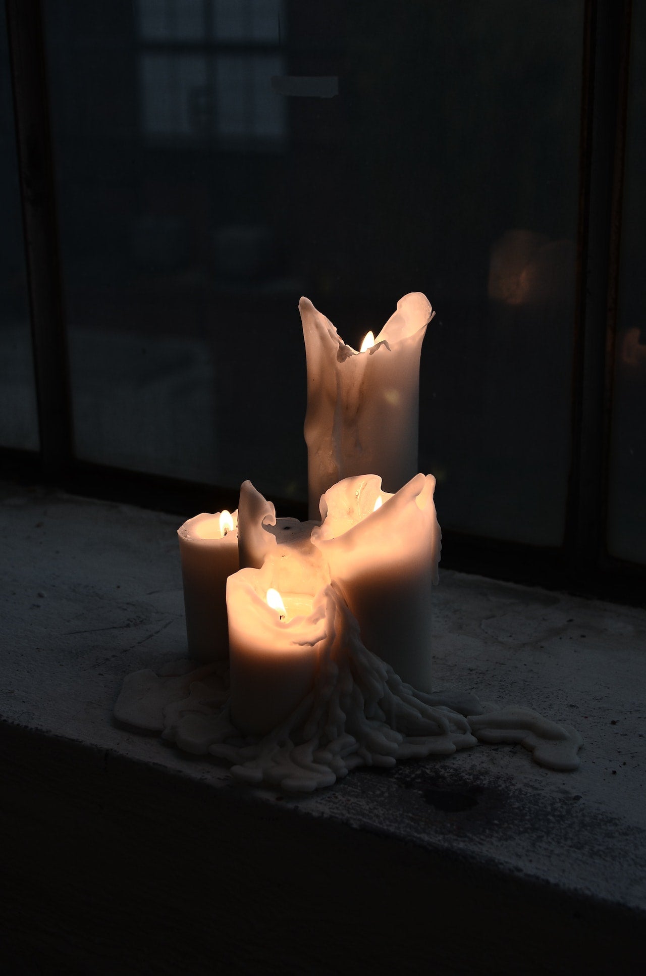 Four white lit candles. One tall candle and three candles half the hight and all of them melted down the sides with wax onto the table.