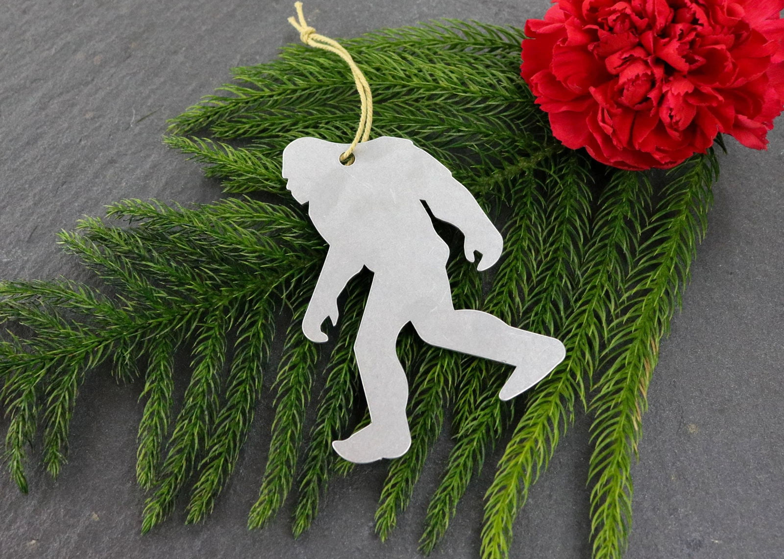 Bigfoot metal ornament with evergreen branches and a red carnation.