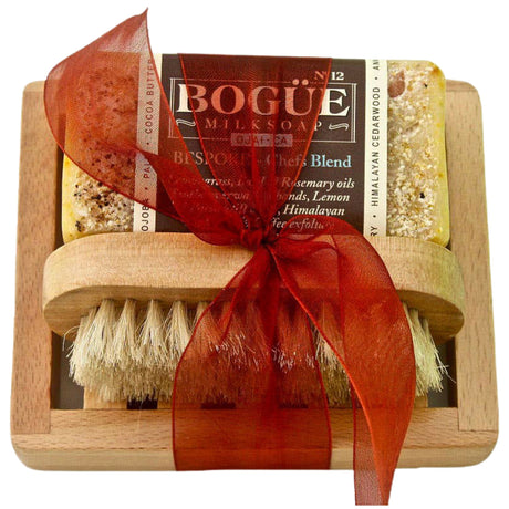 Gift set containing two bars of Bogue Goat Milk Soap and a wooden soap dish. The soap bars have a brown color and are tied together with a red ribbon. The soap dish has a rectangular shape with raised sides.