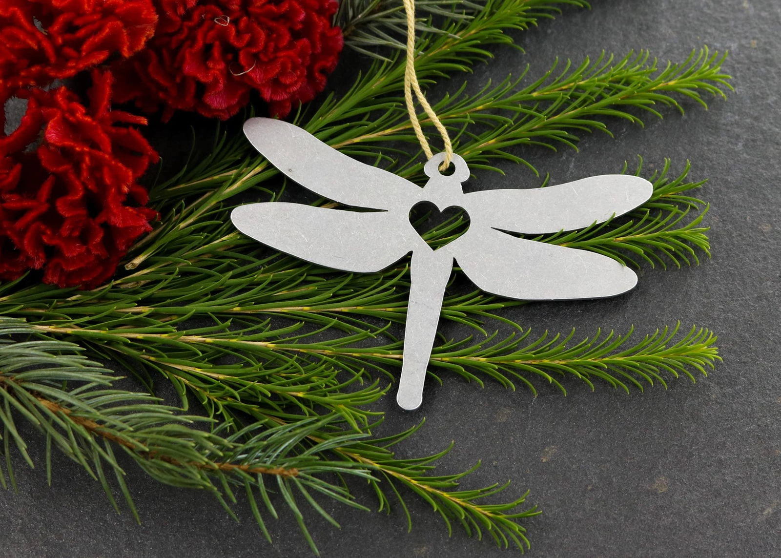 Dragonfly metal ornament with heart cutout, surrounded by greenery.