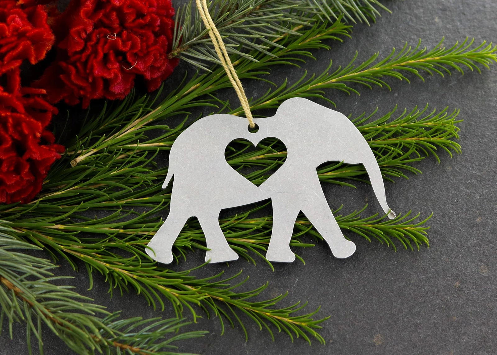 Elephant metal ornament with heart cutout, surrounded by greenery and red flowers.