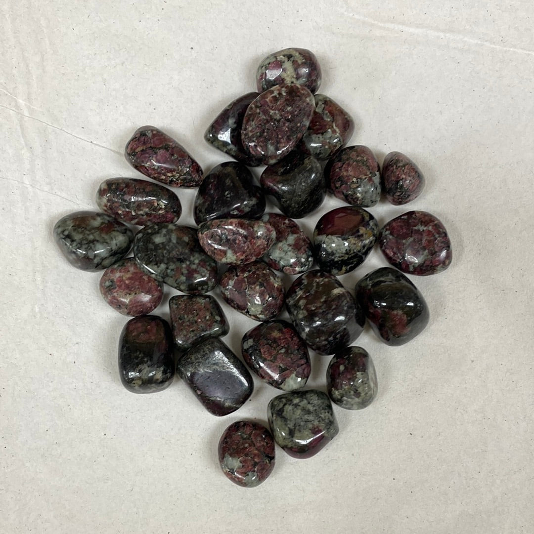 A cluster of tumbled Eudialyte stones with a smooth, polished finish. The stones exhibit a vibrant mix of deep red, black, and white colors, with a speckled and translucent appearance.