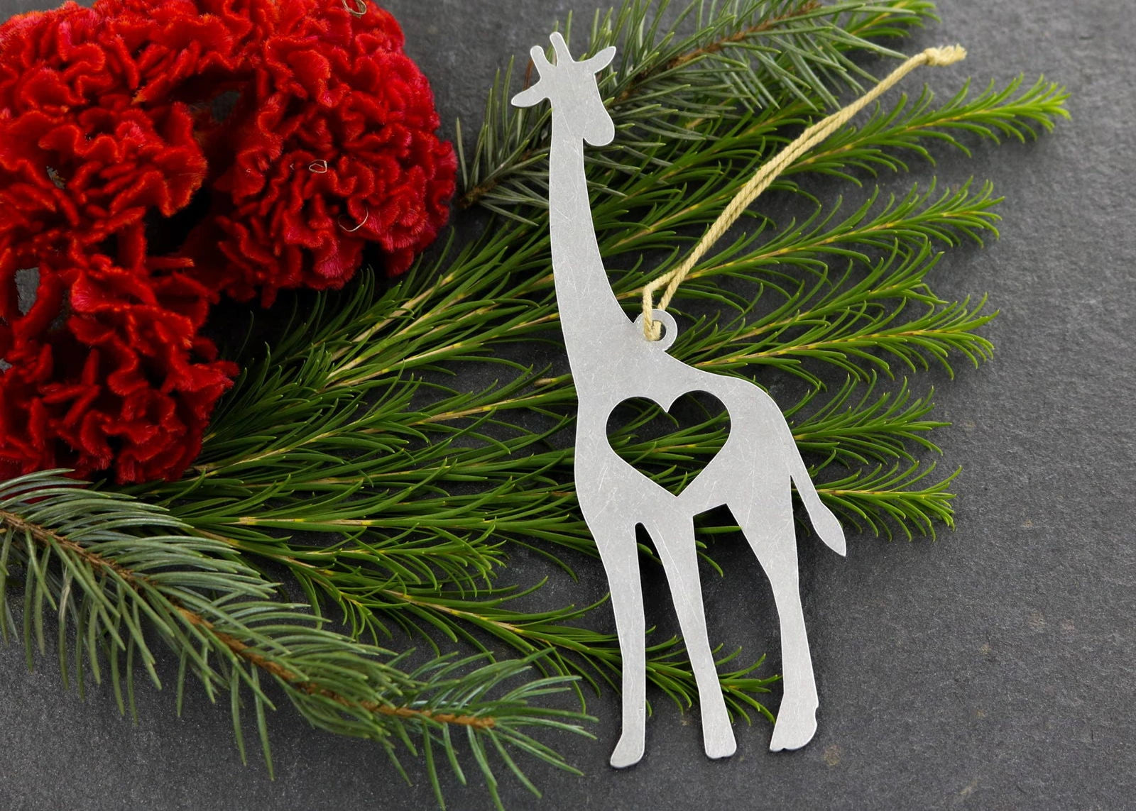 Giraffe metal ornament with heart cutout, surrounded by greenery and red flowers.