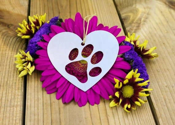 Heart-shaped metal ornament with paw print cutout, surrounded by flowers.