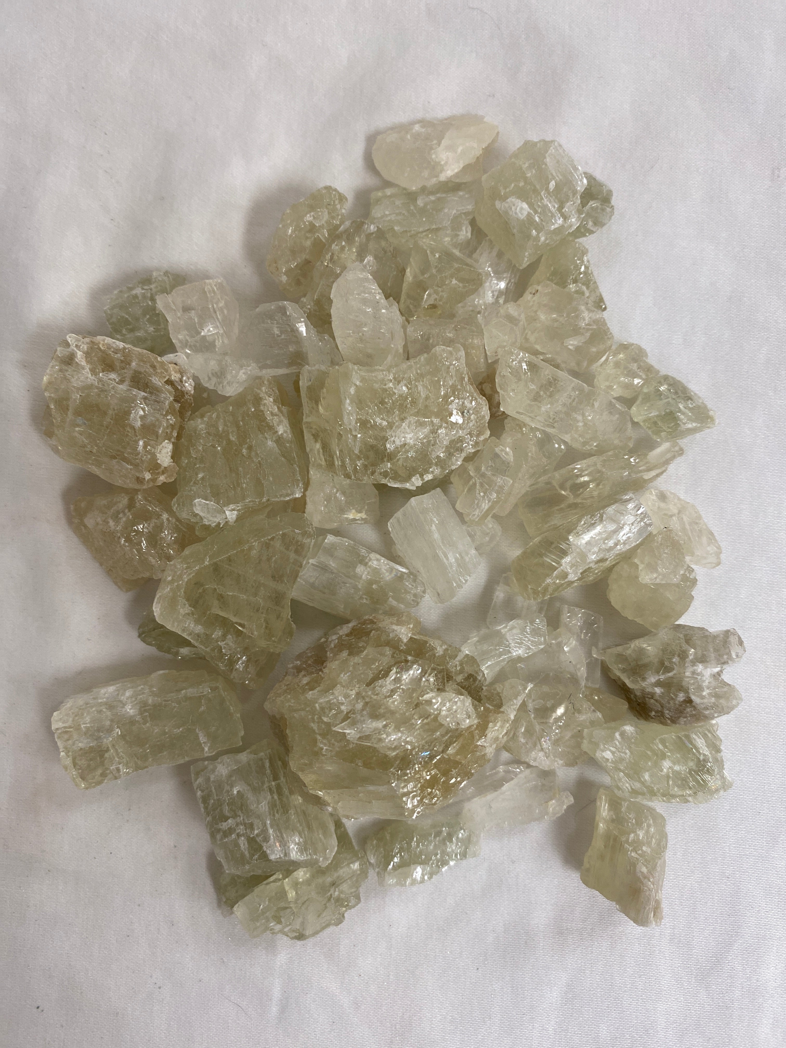 A cluster of raw Hiddenite stones with a natural, rough texture and a vibrant green color. The stones are irregular in shape and size, with some showing signs of cleavage and others with smooth, rounded surfaces.