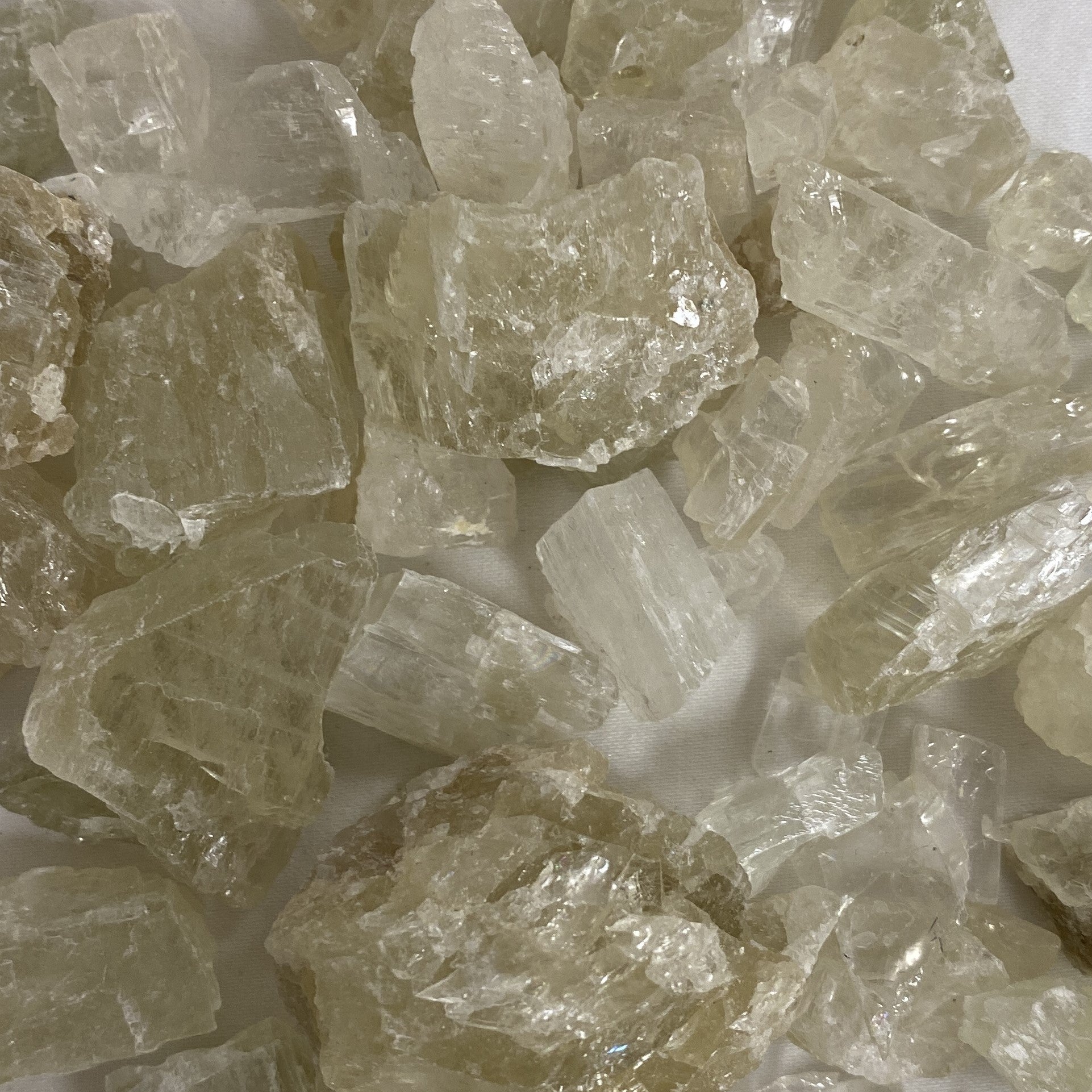 Close-up of a cluster of raw Hiddenite stones with a natural, rough texture and a vibrant green color. The stones are irregular in shape and size, with some showing signs of cleavage and others with smooth, rounded surfaces.