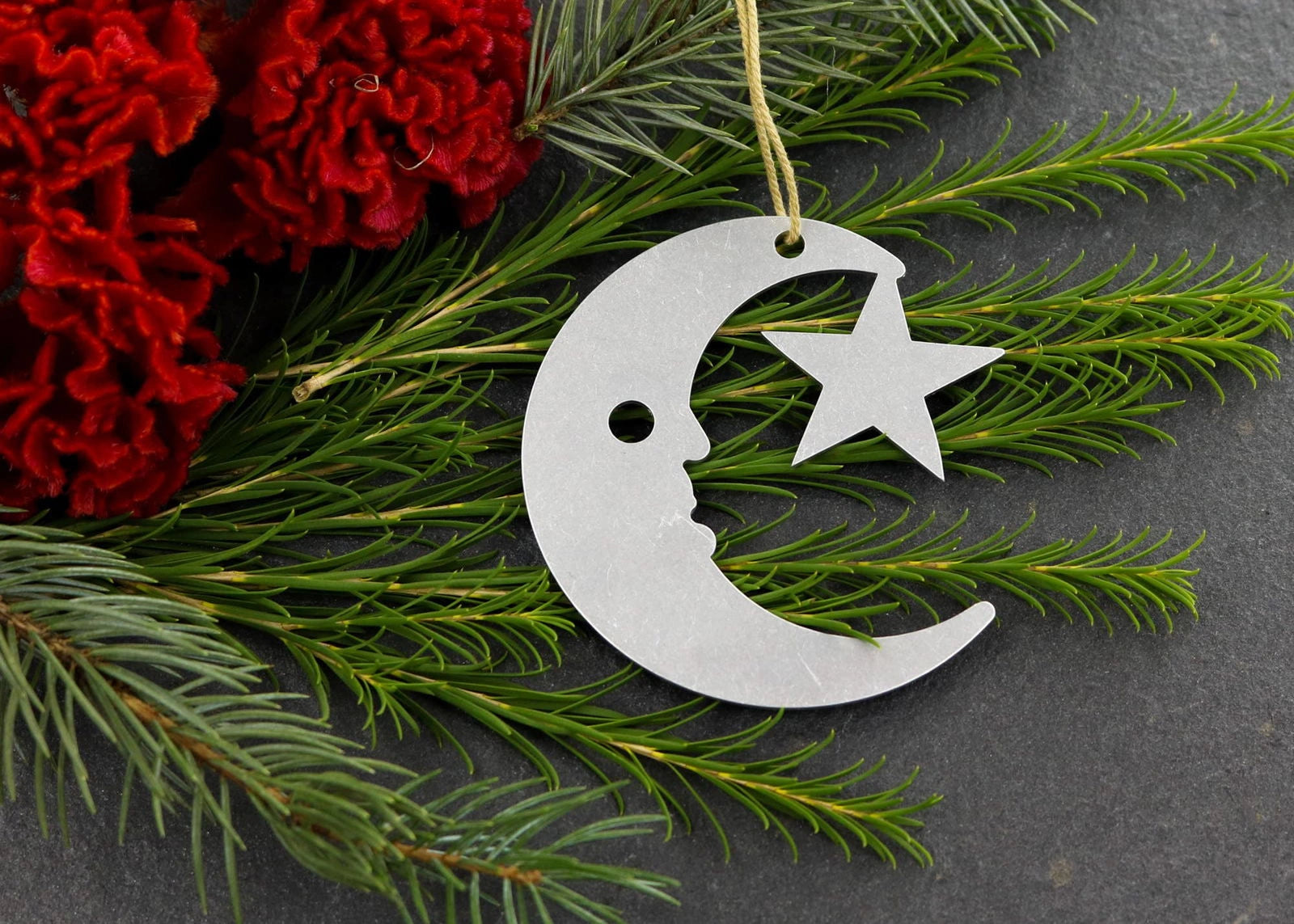 Moon and star metal ornament with greenery and red flowers.