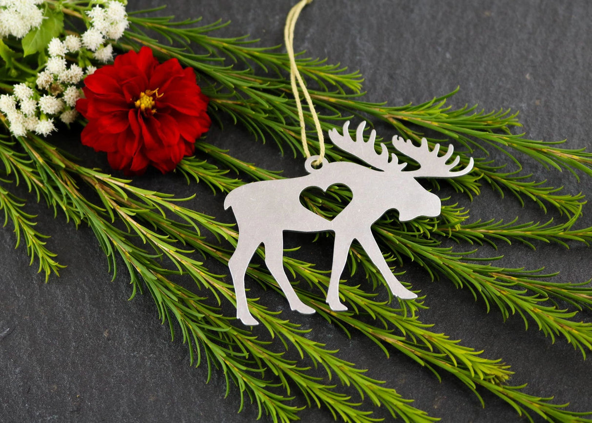 Moose metal ornament with heart cutout, surrounded by greenery and flowers.