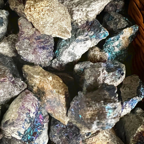 A cluster of raw Peacock Ore stones with a rough, natural finish and a vibrant iridescent color that shifts between shades of blue, green, purple, and brown.