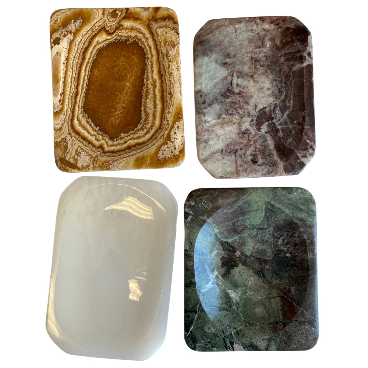 Four small, rectangular stone dishes in various colors and patterns. The top left dish is brown with white swirls, the top right dish is gray with brown and white swirls, the bottom left dish is white with a smooth surface, and the bottom right dish is green with brown and white swirls.