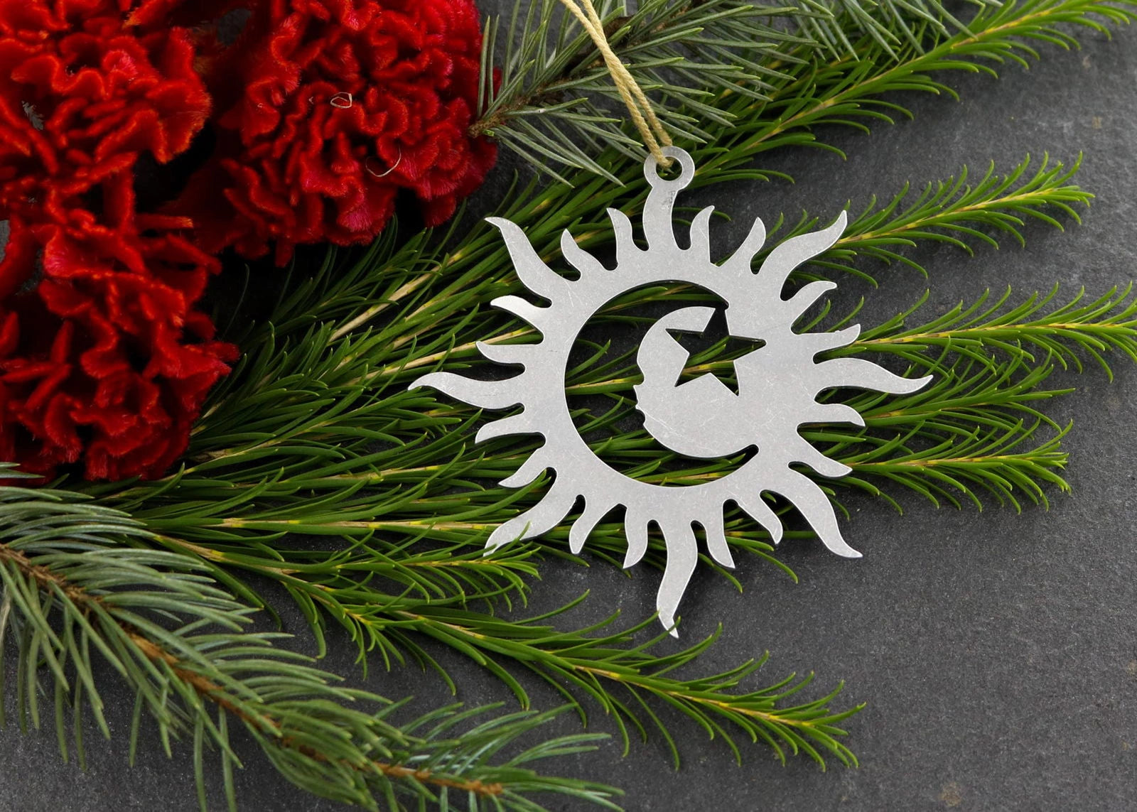 Sun, moon, and star metal ornament with greenery and red flowers.