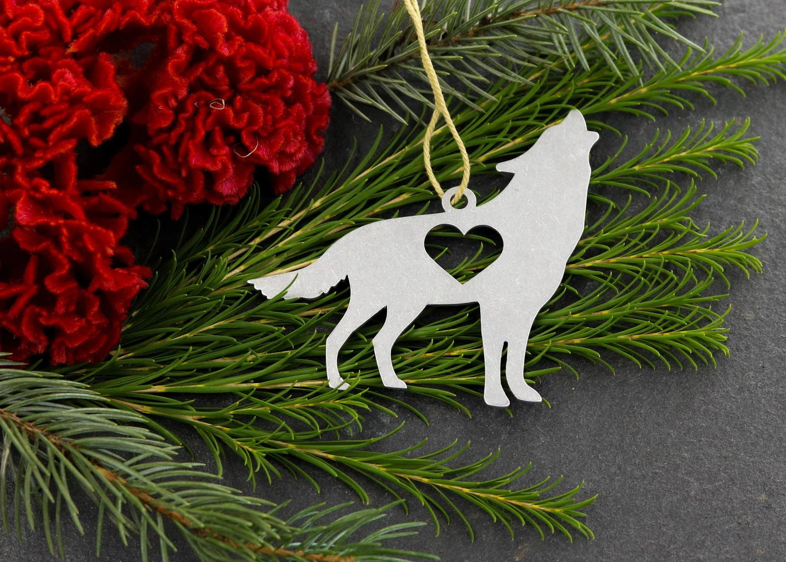 Wolf metal ornament with heart cutout, surrounded by greenery and red flowers.